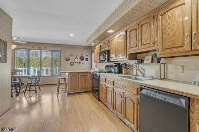 kitchen featuring light countertops, light wood-style flooring, a peninsula, black appliances, and a sink