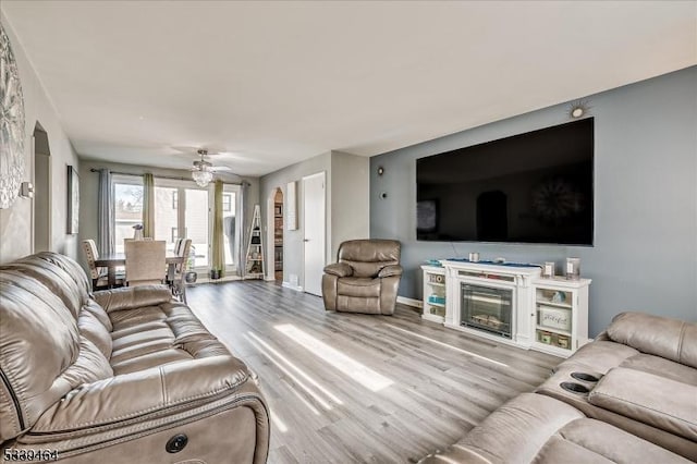 living room with arched walkways, wood finished floors, a ceiling fan, baseboards, and a glass covered fireplace