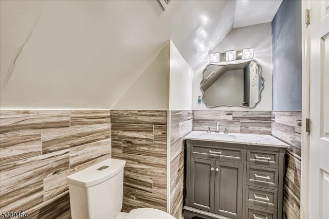 half bath with toilet, lofted ceiling, tile walls, and vanity