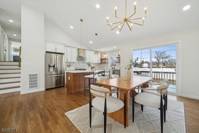 dining space featuring a chandelier, high vaulted ceiling, wood finished floors, visible vents, and stairway