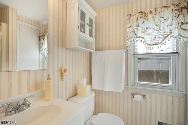 bathroom featuring toilet, wallpapered walls, visible vents, and vanity