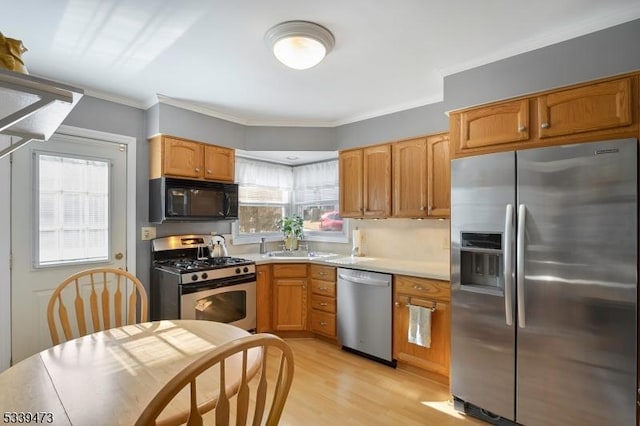 kitchen featuring appliances with stainless steel finishes, light countertops, crown molding, and light wood finished floors