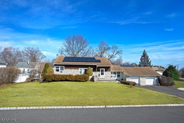 view of front facade with a garage, aphalt driveway, roof mounted solar panels, and a front lawn