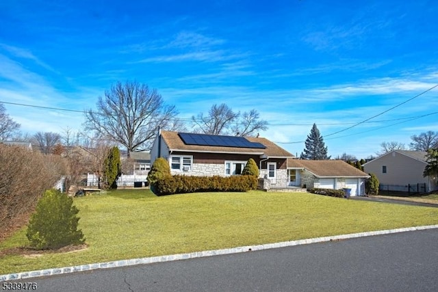 view of front of home featuring a garage, stone siding, roof mounted solar panels, and a front yard