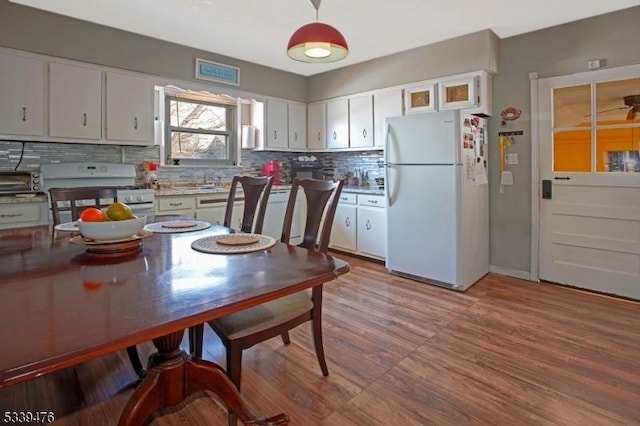 kitchen featuring white appliances, wood finished floors, white cabinetry, and decorative backsplash