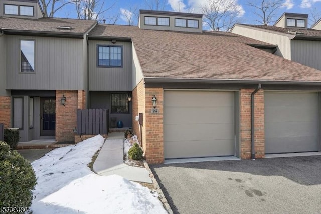 multi unit property with brick siding, driveway, an attached garage, and roof with shingles