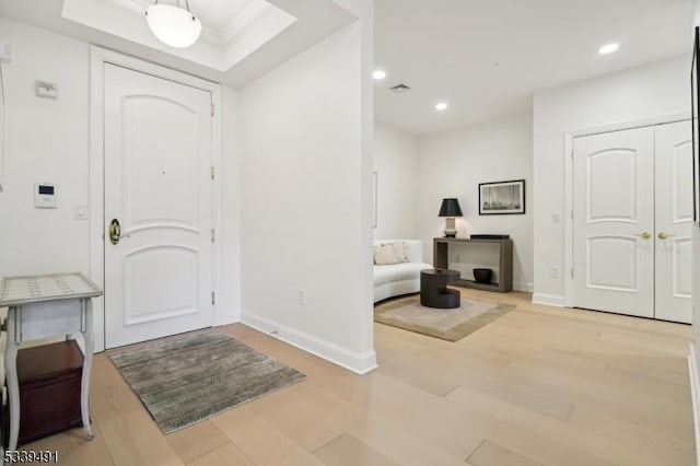 foyer with a raised ceiling, recessed lighting, light wood-style floors, and baseboards