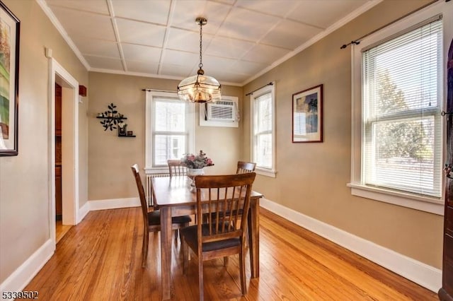 dining room featuring a wall mounted AC, baseboards, crown molding, and wood finished floors