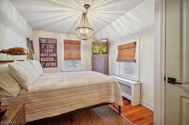 bedroom featuring a chandelier, radiator, wood finished floors, and baseboards