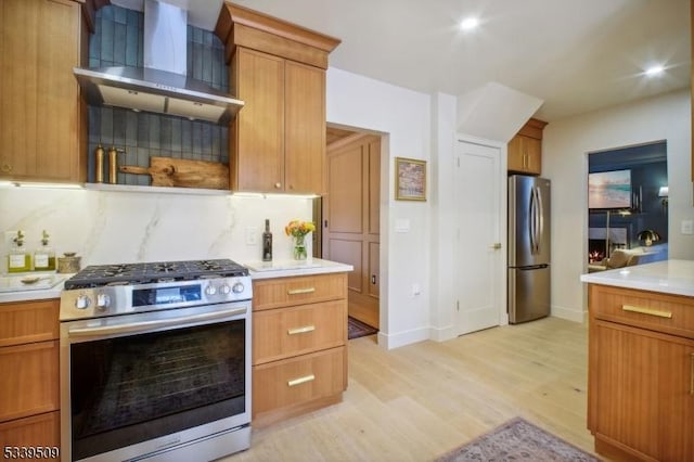 kitchen with light wood finished floors, tasteful backsplash, wall chimney exhaust hood, stainless steel appliances, and light countertops