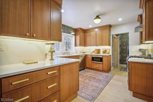 kitchen with stainless steel appliances, a sink, light countertops, light wood finished floors, and brown cabinetry