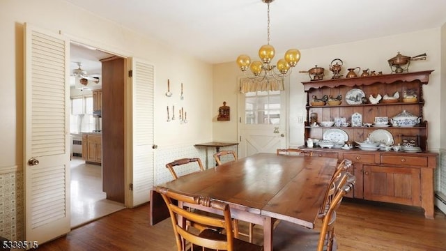 dining space featuring radiator, dark wood-type flooring, and ceiling fan with notable chandelier