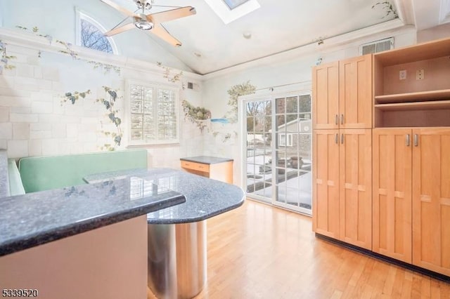 kitchen with open shelves, vaulted ceiling with skylight, a wealth of natural light, and light wood-style floors