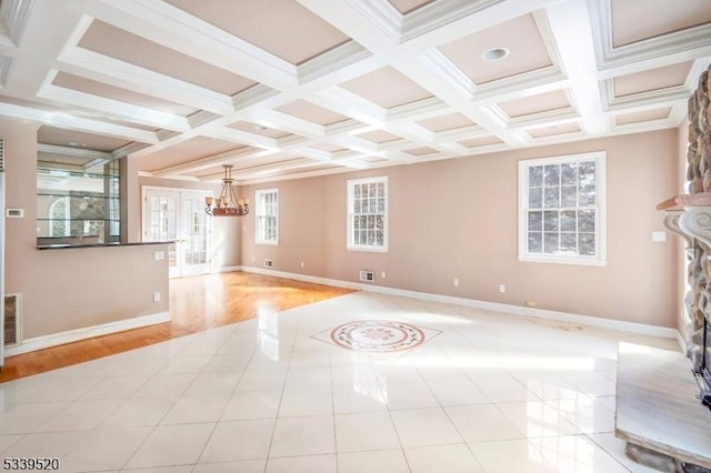 unfurnished living room featuring baseboards, coffered ceiling, an inviting chandelier, a stone fireplace, and beam ceiling