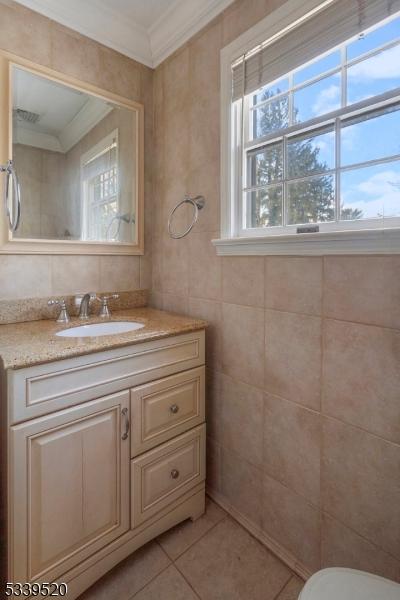 bathroom with tile patterned floors, tile walls, crown molding, and vanity