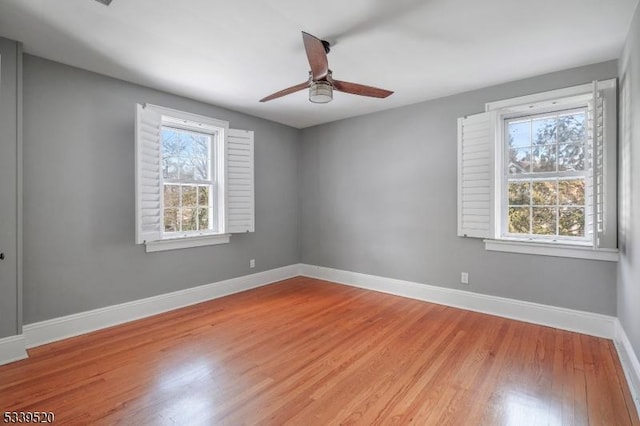 empty room with a ceiling fan, plenty of natural light, light wood-style flooring, and baseboards