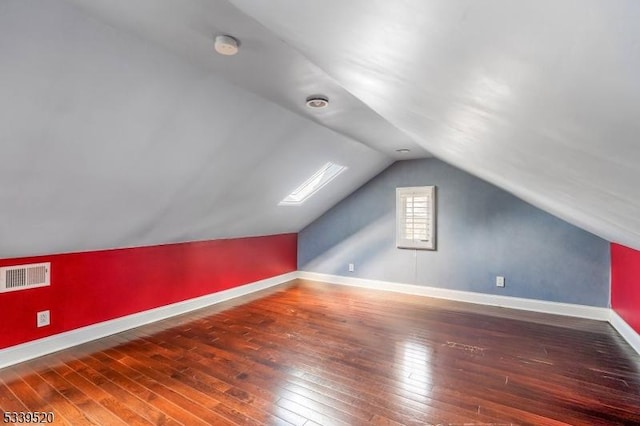 additional living space with dark wood-style flooring, visible vents, vaulted ceiling, and baseboards