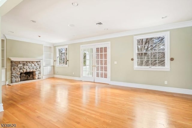 unfurnished living room with ornamental molding, baseboards, a stone fireplace, and built in features