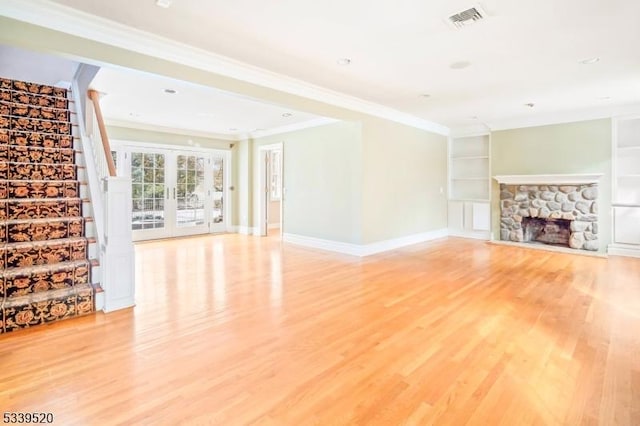 unfurnished living room featuring visible vents, ornamental molding, stairs, light wood-type flooring, and built in shelves