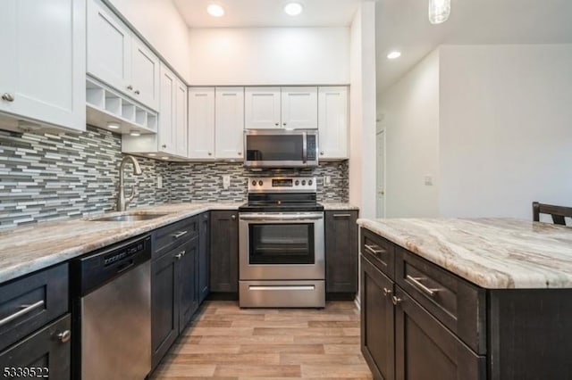 kitchen with stainless steel appliances, white cabinetry, a sink, and light stone counters