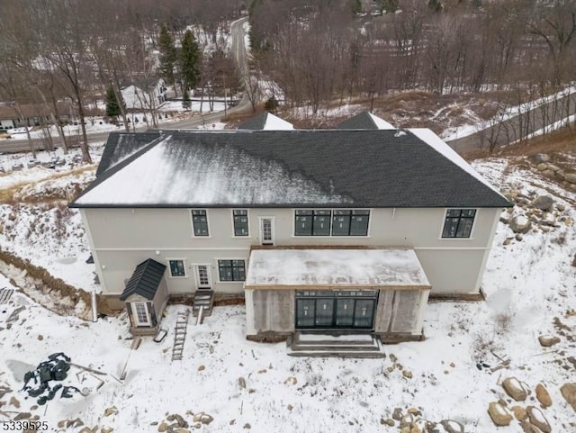 snow covered house featuring entry steps and a shingled roof