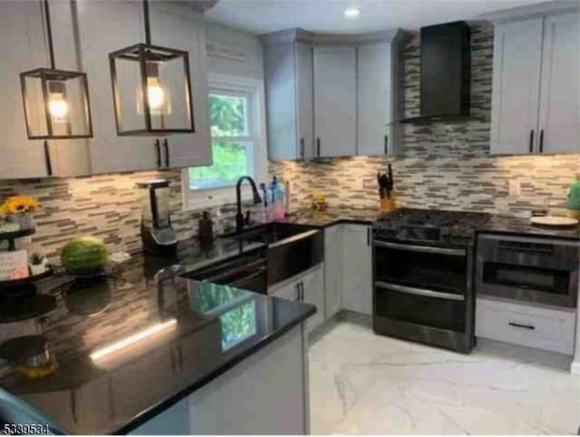 kitchen featuring tasteful backsplash, dark countertops, hanging light fixtures, marble finish floor, and wall chimney range hood