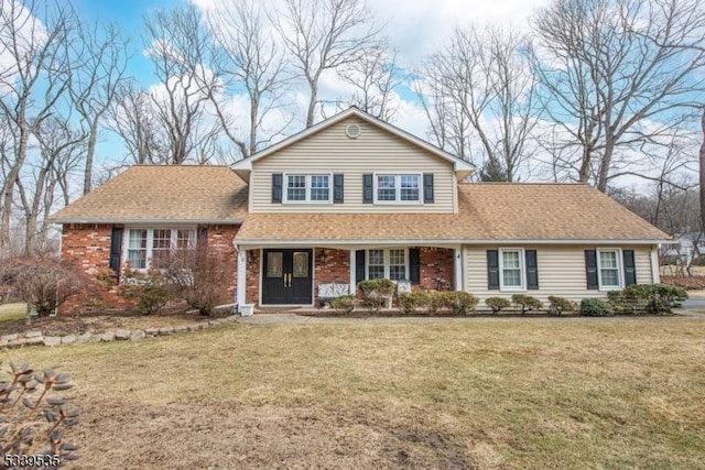 view of front facade featuring a shingled roof, covered porch, brick siding, and a front lawn