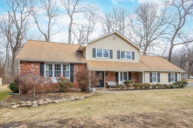 view of front of property featuring a shingled roof, a front lawn, and brick siding