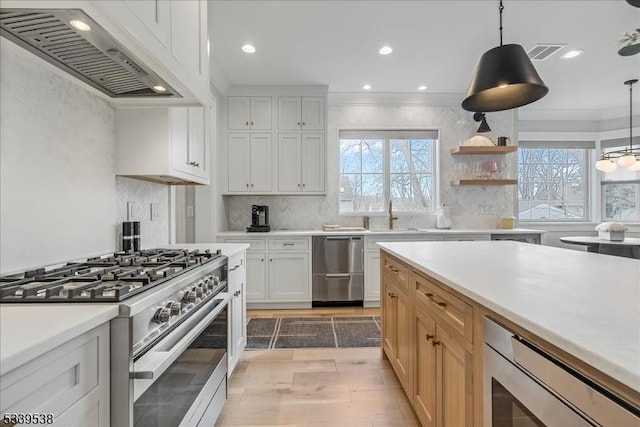 kitchen featuring visible vents, light countertops, appliances with stainless steel finishes, wall chimney range hood, and decorative backsplash