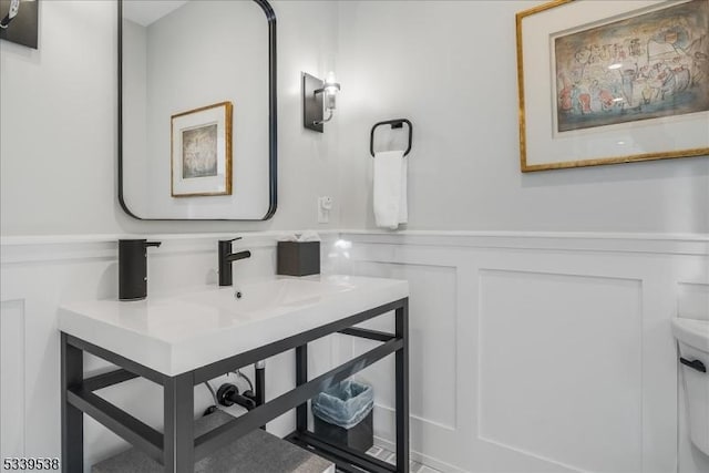 bathroom featuring toilet, wainscoting, vanity, and a decorative wall