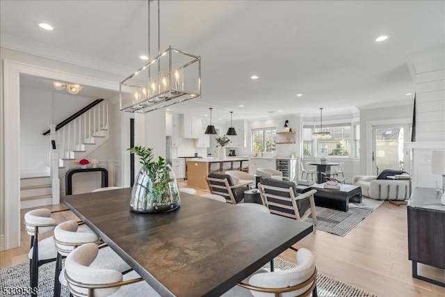 dining space featuring beverage cooler, light wood-style flooring, ornamental molding, stairs, and recessed lighting