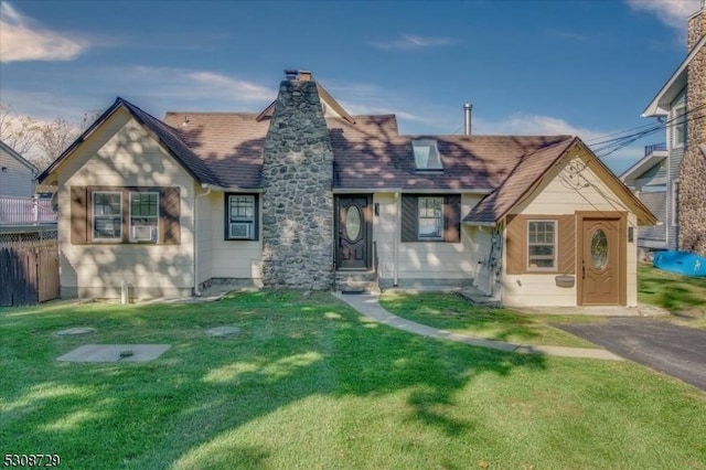 english style home featuring roof with shingles, a chimney, a front yard, and fence