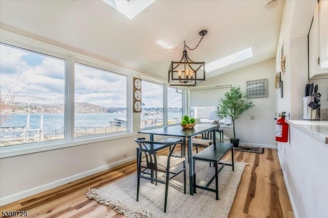 dining space featuring lofted ceiling with skylight, light wood-type flooring, a water view, and an inviting chandelier