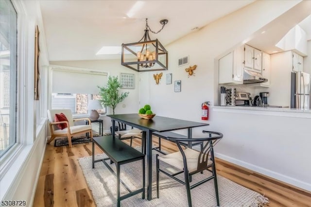 dining space with light wood-style floors, a chandelier, visible vents, and vaulted ceiling