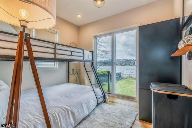 bedroom with light wood-type flooring, a water view, and multiple windows