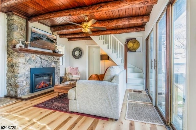 living area with a fireplace, stairway, light wood-style floors, wooden ceiling, and beamed ceiling