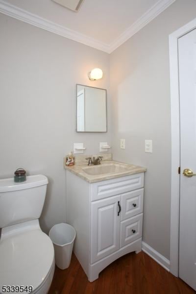 bathroom with toilet, wood finished floors, vanity, baseboards, and ornamental molding