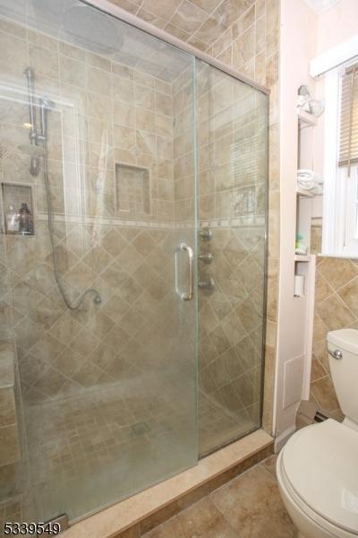 bathroom with tile patterned floors, a shower stall, toilet, and tile walls