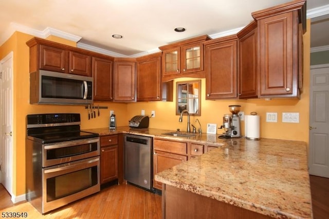 kitchen featuring brown cabinets, appliances with stainless steel finishes, a sink, light stone countertops, and a peninsula