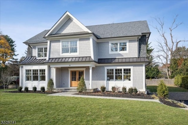 view of front facade with a standing seam roof, metal roof, fence, and a front lawn