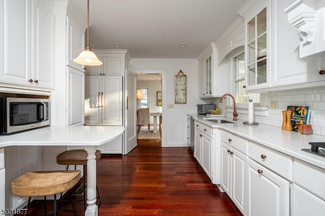 kitchen with light countertops, stainless steel microwave, hanging light fixtures, glass insert cabinets, and white cabinets