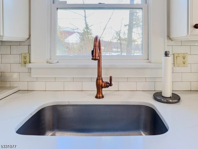 details with light stone counters, white cabinetry, a sink, and decorative backsplash