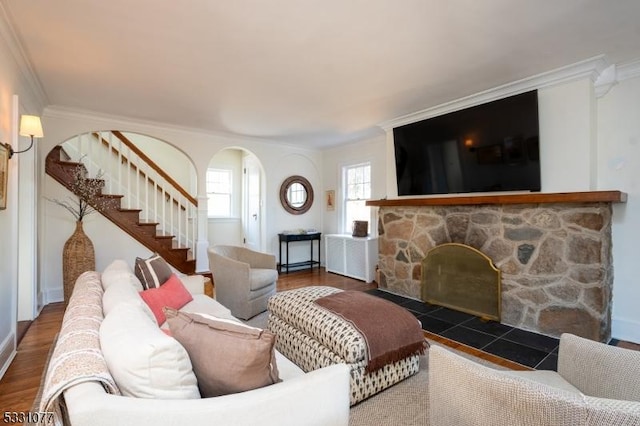 living area featuring arched walkways, crown molding, a fireplace, wood finished floors, and stairs