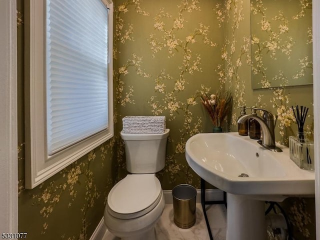 bathroom with baseboards, a healthy amount of sunlight, toilet, and wallpapered walls