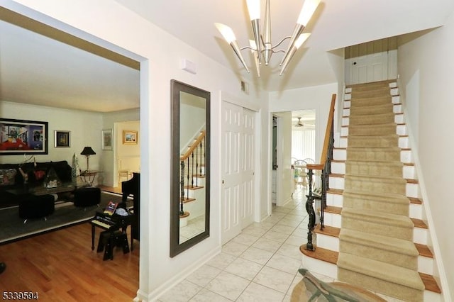 hall with stairs, light tile patterned flooring, baseboards, and a chandelier