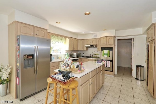 kitchen with light brown cabinetry, appliances with stainless steel finishes, a center island, light countertops, and under cabinet range hood