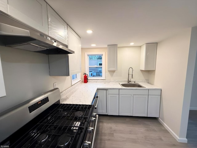 kitchen featuring under cabinet range hood, wood finished floors, a sink, baseboards, and gas stove