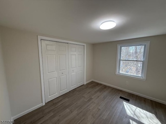 unfurnished bedroom featuring a closet, wood finished floors, visible vents, and baseboards