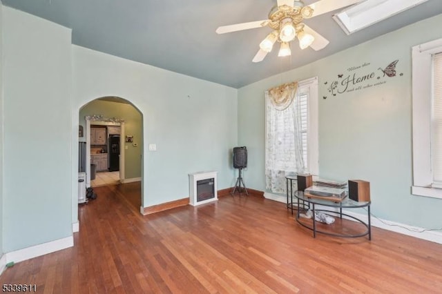 sitting room with arched walkways, wood finished floors, a ceiling fan, and baseboards