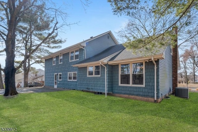 back of house with a shingled roof, a lawn, a chimney, and central AC unit